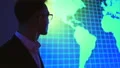 The man in glasses standing near a screen with the world map 4k or 4k+ Resolution