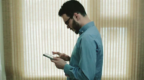 A man in glasses standing near a  window with a tablet Stock Footage 62441905