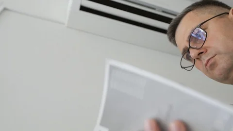 A man with glasses standing next to a working air conditioner is studying the Stock Footage 109351650
