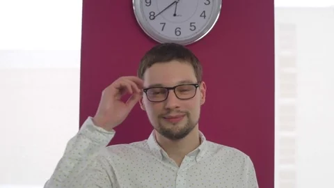 Man with glasses stands on the background with a clock Stock Footage 74096927