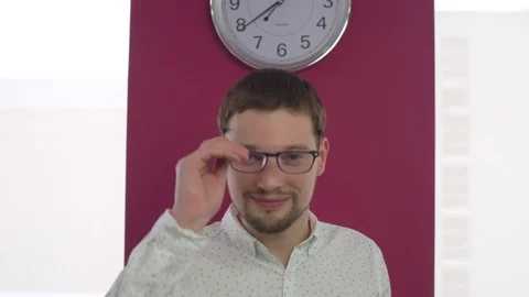 Man with glasses stands on the background with a clock. The office has a window Stock Footage 74097129