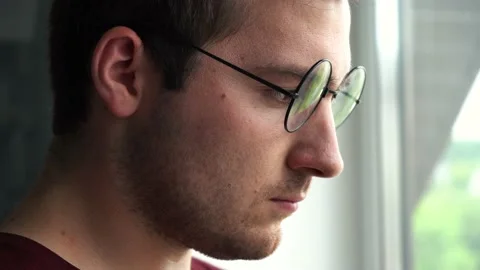 A man with glasses stands by the window and stares 스톡 동영상 158326883