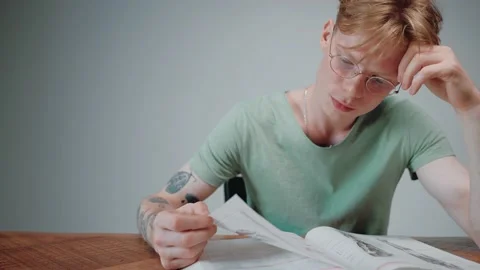 Man in glasses studying and stressing, reading a textbook in empty grey room Vídeo Stock 164372843