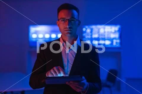 The man in glasses with a tablet working in a room with screens Stock Photos