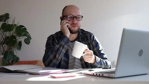 Man with glasses talking on the phone while sitting at a table in the office. Video stock 243372689