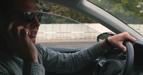A man with glasses is talking while driving a car in motion. Stock Footage 154332098