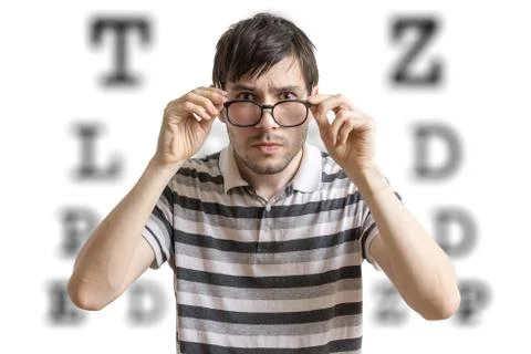 Man with glasses is testing his sight. Chart for eye sight testing in background 스톡 사진