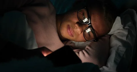 Man in glasses text messaging using mobile phone in bed Stock Footage 145291301