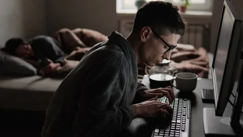 Man in glasses typing intensely on a computer in a dim home bedroom workspace Video stock 307691843