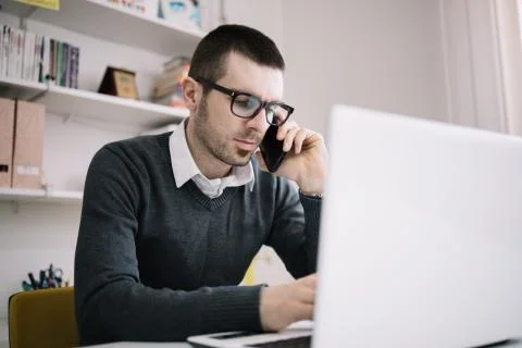 Man with glasses using phone while sitting at office desk Stock Photos