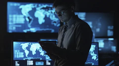 Man in glasses is using a smartphone in a dark monitoring room with displays Stock Footage 59378748