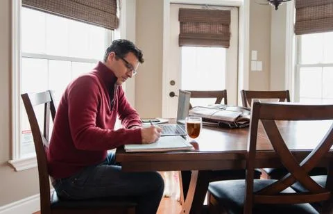Man in glasses working from home using a computer at a dining table. Foto stock