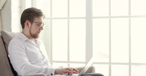 Man in glasses is working typing on laptop in office near window, side view. Stock Footage 132100540