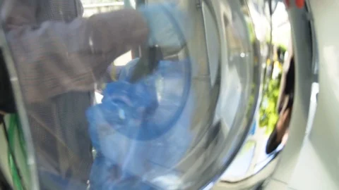A man with gloves loads a washing machine with laundry Stock Footage 117432485