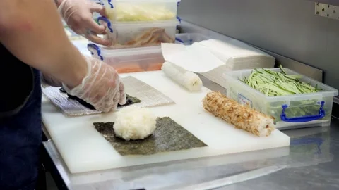 Man in gloves is making a sushi roll with black rice using bamboo mat. Closeup Stock Footage 131598469