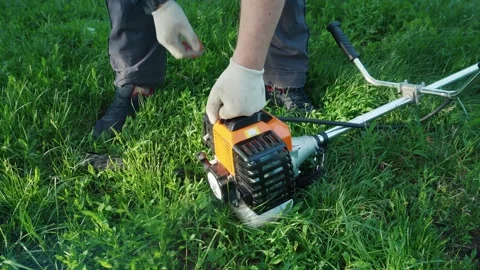 A man in gloves starts the engine of a gasoline trimmer while standing on green Stock Footage 336870811