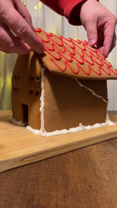 Man glues with red wave pattern, edible paint roof to gingerbread house 스톡 동영상 320981741