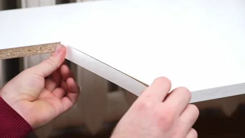 A man glues white melamine edging to raw edge of wood chipboard furniture. Stock Footage 168217523