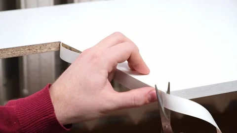 A man glues white melamine edging to raw edge of wood chipboard furniture. 库存影片 168648119