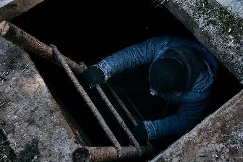A man go down into the cellar along an iron ladder. People climbs a ladder fr Stock Photos