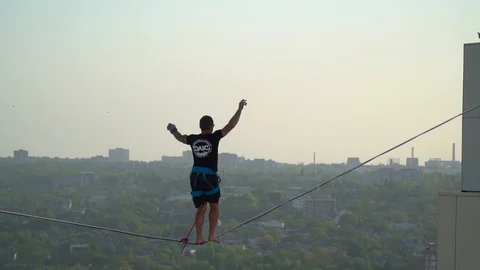 A man goes balancing on a tightrope to the edge of a skyscraper Stock Footage 90281485