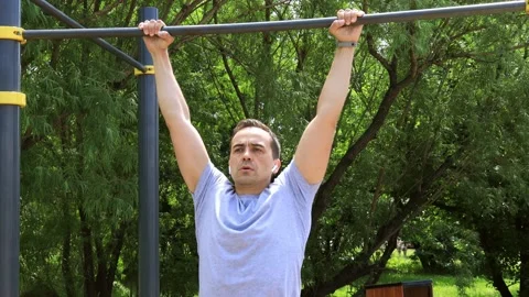 A man goes in for sports pulls himself up on the horizontal bar in the park Stock Footage