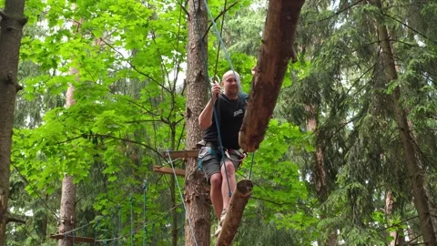A man goes through a difficult obstacle course on suspended logs at a height Stock Footage 337183330
