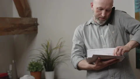 Man goes through his stack of mail while talking on the phone in his home office 動画素材 133296293