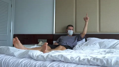Man going crazy in quarantine laying down in bed in a face mask shooting fingers Stock Footage 158430871