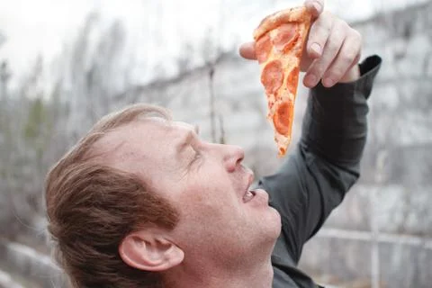 The man is going to eat pizza. It's in the open air. Holding a piece of pizza Stock Photos