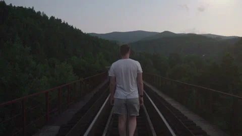 Man going on the railway on the bridge into the mountains at dusk in Slow Motion Video stock 160770486