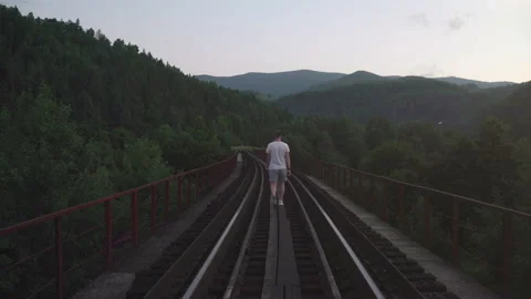 Man going on the railway on the bridge into the mountains at dusk Stock Footage 160770529