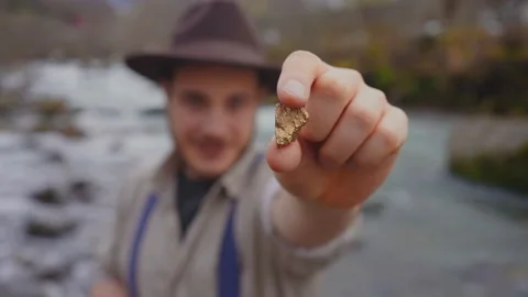 Man gold digger in a hat shows a large gold nugget to the camera Stock Footage 233976305