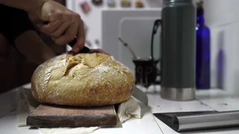 Man grabs knife and cuts a sourdough loaf in half in the kitchen Stock Footage 201761039