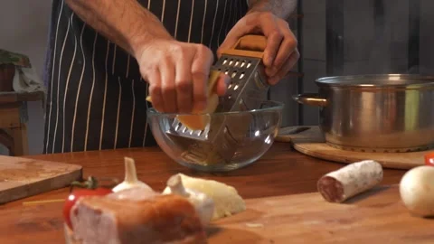 A man grates cheese against the backdrop of a kitchen interior and surrounded by Stock-Footage 259149135