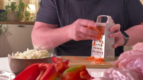 A man grates raw carrots in the kitchen, foreground Stock Footage 304795562