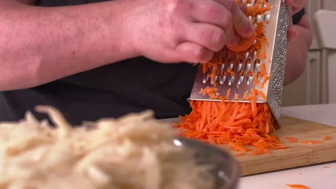 A man grates raw carrots in the kitchen, foreground Vídeo Stock 304795623