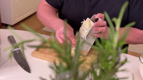 A man grates raw potatoes in the kitchen, foreground Stock Footage 304794105