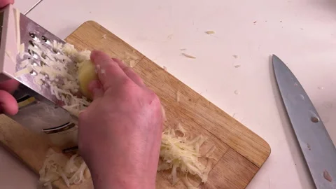 A man grates raw potatoes in the kitchen, foreground Vídeo Stock 304795430