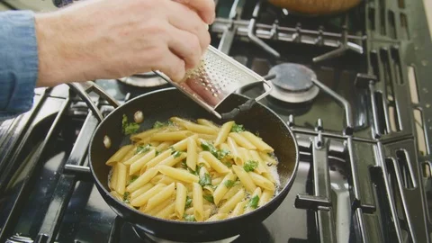 Man Grating Cheese Over Penne Pasta In Skillet On Stove Stock Footage 86071838