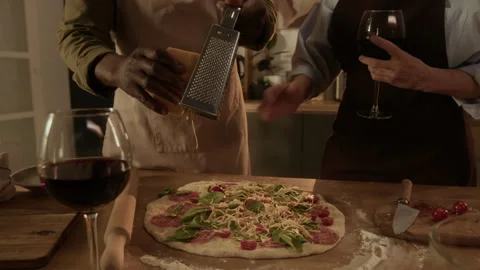 Man Grating Cheese over Pizza Dough, His Wife Watching Him with Glass of Wine Vídeo Stock 312808452