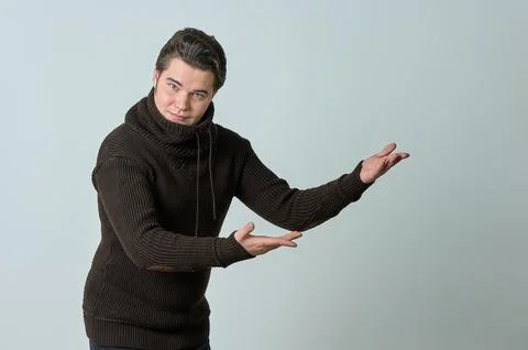 A man on a gray background in a brown sweater showing emotions, shows his hands. Stock Photos