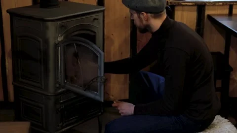 Man in gray cap and black sweater interacts with a wood stove Stock-Footage 319963003