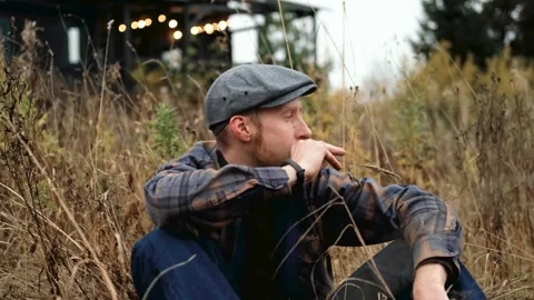 Man with a gray cap sits thoughtfully among tall grass Stock Footage 319962318