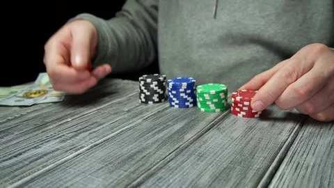 A man in gray clothes rolls dice on a wooden table, and cash and poker chips are Stock Footage 330536571
