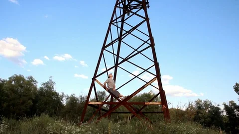 A man in gray clothes is sitting on a rusty old high-voltage pole Video stock 100250656