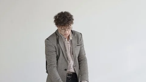A man in a gray jacket and glasses stands in a white room and meditates Stock Footage 124941768
