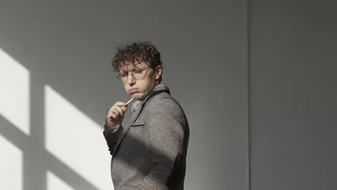 A man in a gray jacket and glasses stands in a white room and meditates Stock Footage 124941990