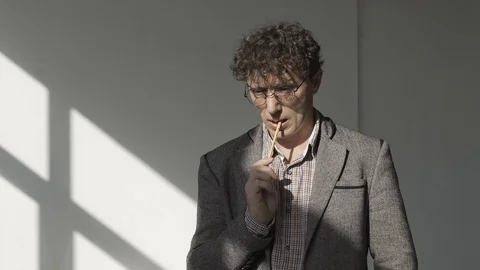 A man in a gray jacket and glasses stands in a white room and meditates Stock Footage 124942189