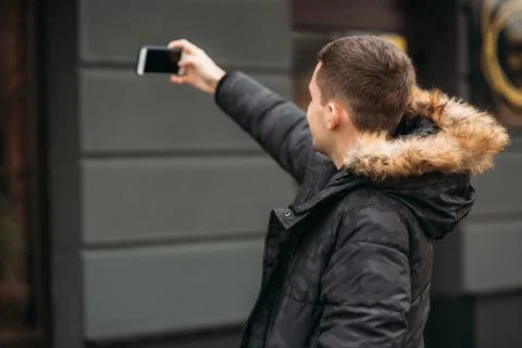 Man in a gray jacket is standing outside and using a phone Stock Photos